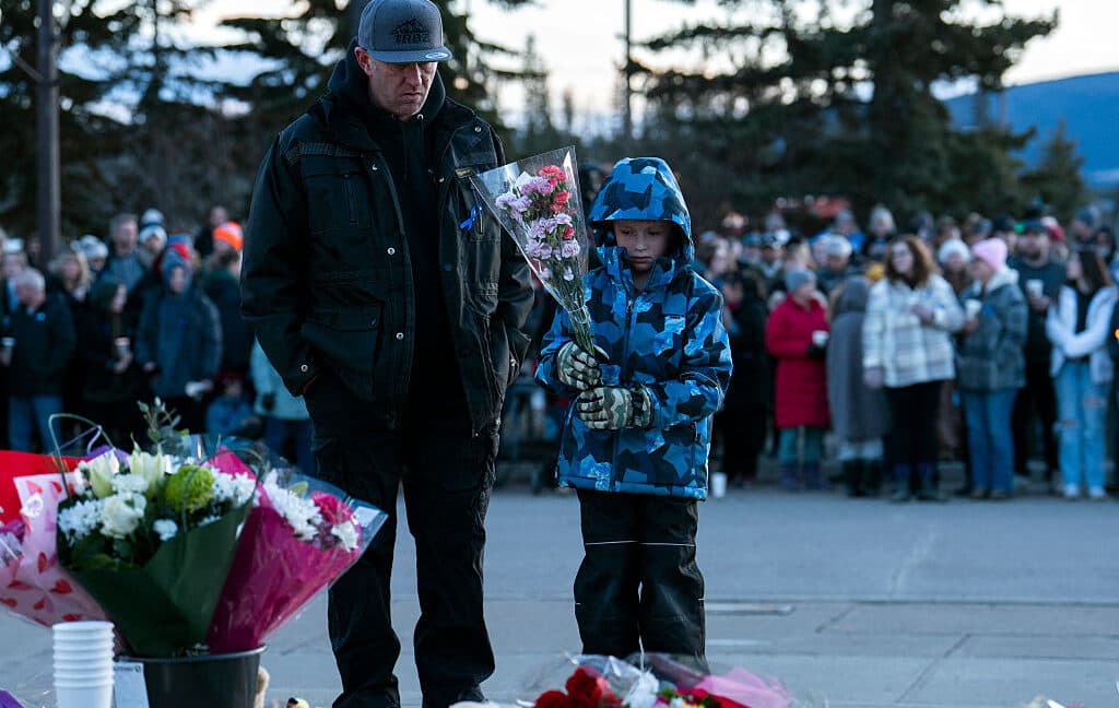Flowers and candles at a school memorial next to a laptop showing an AI chatbot interface